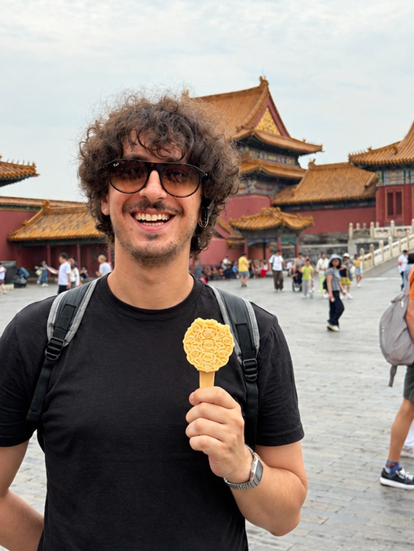 Giacomo smiling in front of the Forbidden City in Beijing, holding a pastry
