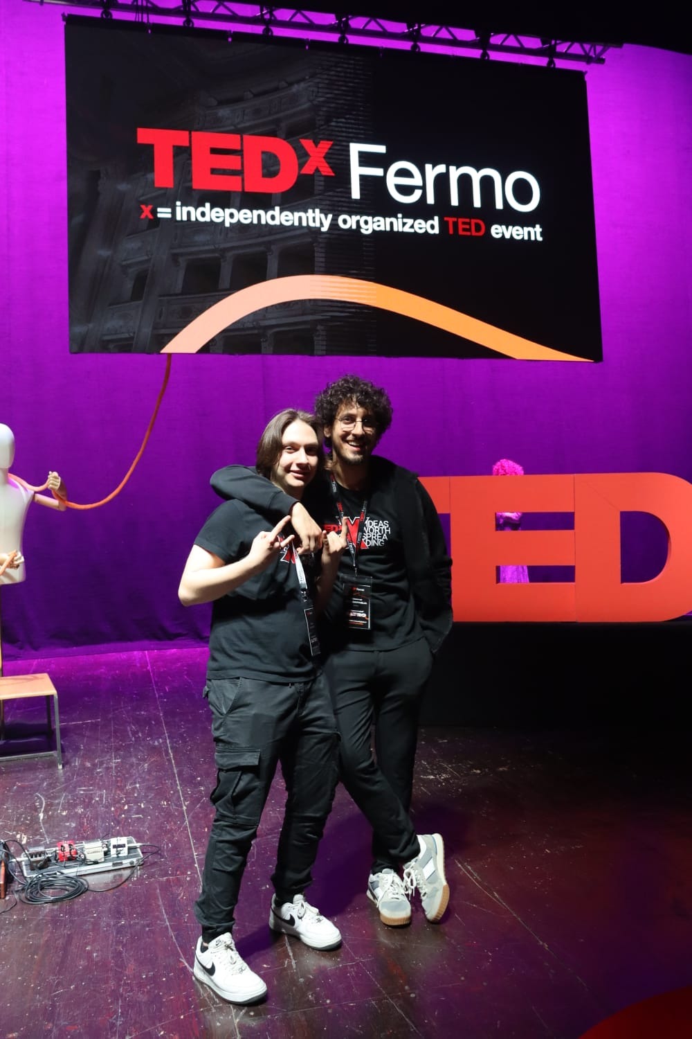 Giacomo with a friend on the TEDx Fermo stage, in front of the event backdrop